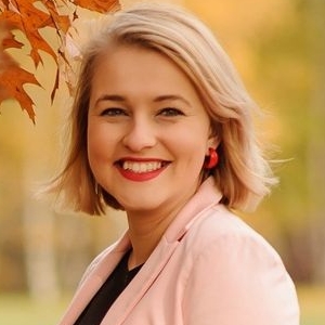 Zdjęcie portretowe: Uśmiechnięta Ola szalek-palmowska. Krótkie blond włosy, usta pomalowane na czerwono.