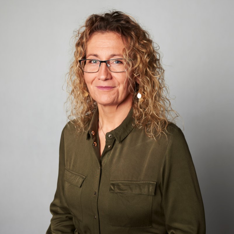 Zdjęcie portretowe: Anna Brzegowa Jabczyk. Długie kręcone włosy. Ubrana w koszulę, na nosie okulary. Patrzy w obiektyw i uśmiecha się delikatnie.