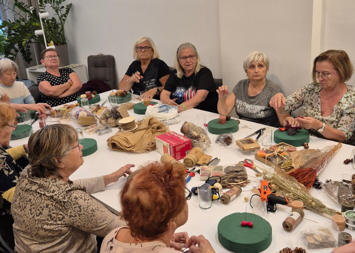Kolorowe zdjęcie w Pracowni Dostępnej Kultury. Zajęcia z robienia jesiennych stroików. Osoby starsze siedzą przy stole i tworzą własne stroiki.