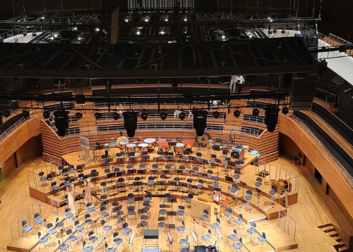 Kolorowe zdjęcie. Scena w Narodowym Forum Muzyki z ustawionymi krzesłami i pulpitami dla orkiestry oraz instrumentami perkusyjnymi w tle. Eleganckie, drewniane wnętrze z nowoczesnym oświetleniem.