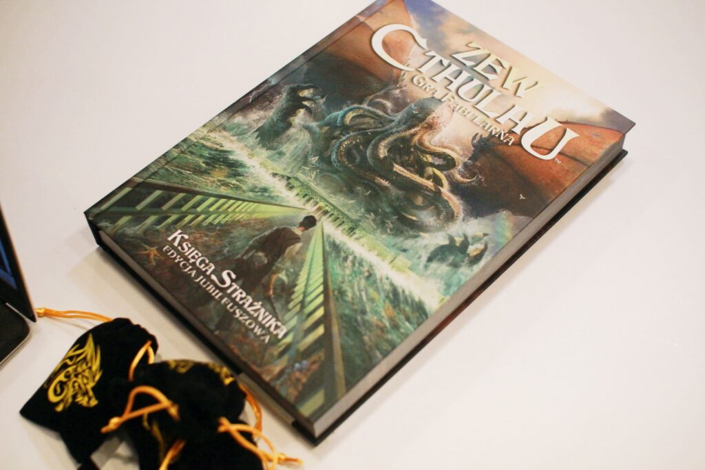 Na zdjęciu okładka gry fabularnej Zew Cthulhu. Grafika w stylu fantasy. Postać przedstawiająca mężczyznę stoi na moście prowadzącym ku wielkiej, bajkowej ośmiornicy.