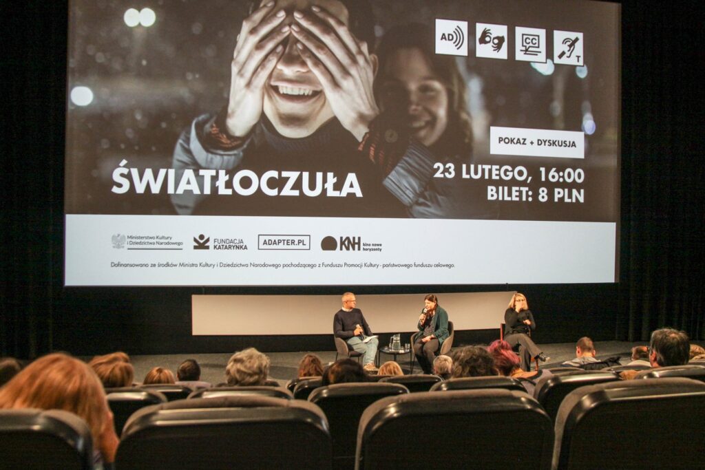 Zdjęcie z sali kinowej. Na ekranie wyświetla się napis Światłoczuła oraz kadr z filmu. Przed ekranem rząd krzeseł kinowych i widownia.