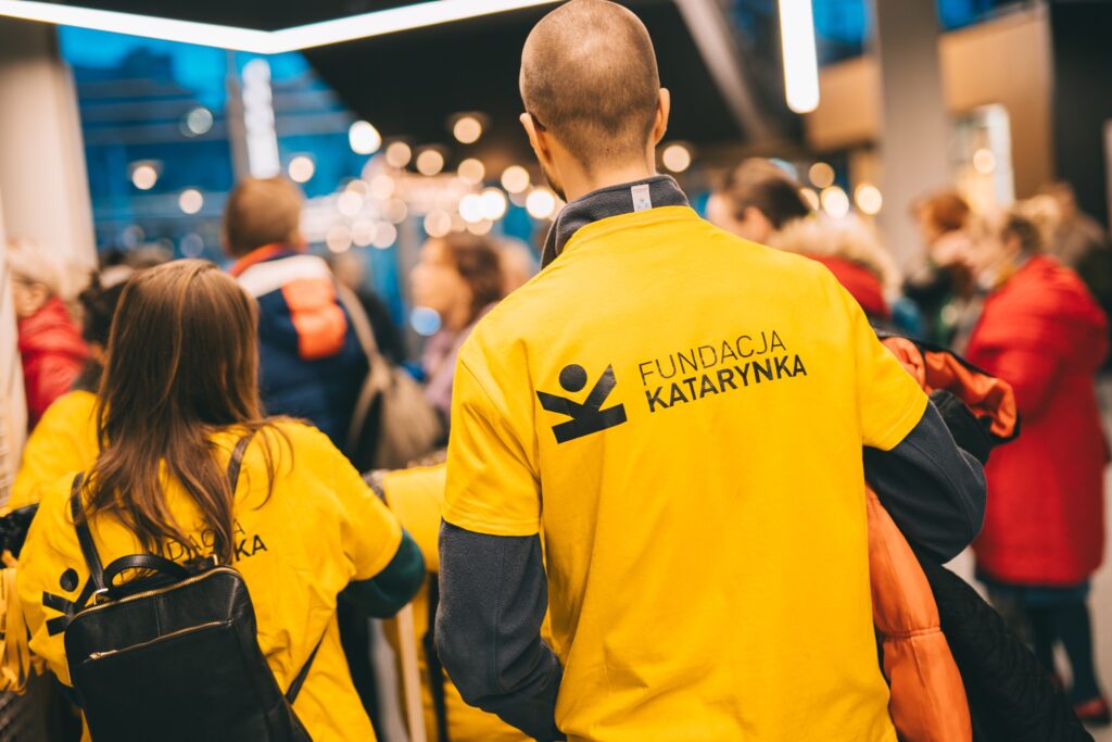 Na zdjęciu dwie osoby w żółtych koszulkach z logiem Fundacja Katarynka. W tle rozmazany tłum osób.